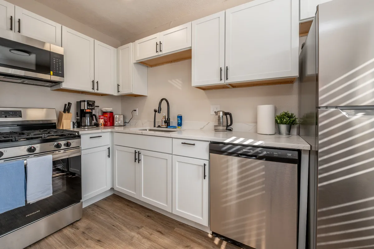 A bright, modern kitchen featuring stainless steel appliances, crisp white cabinetry, a spacious kitchen island, and a large window that lets in abundant natural light. The setup is ideal for cooking and gathering, with plenty of counter space and room for socializing or meal prep.