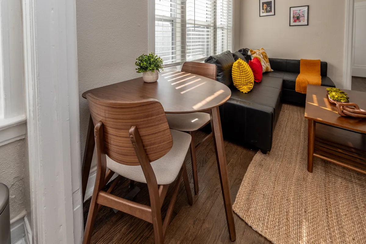 A welcoming dining table adjacent to a comfortable sofa, adorned with decorative cushions and a touch of greenery from a nearby plant. The setup suggests versatility—ideal for intimate dinners, creative brunches, or even using the table as a workspace.