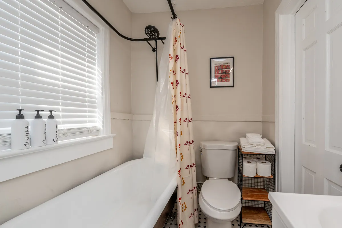 This image shows a bathroom interior featuring a bathtub with a shower curtain, a toilet, a framed picture on the wall, and a sink. The space appears clean and inviting, with amenities laid out for daily use. The scene captures elements of a refreshing morning routine and a relaxing bath experience.