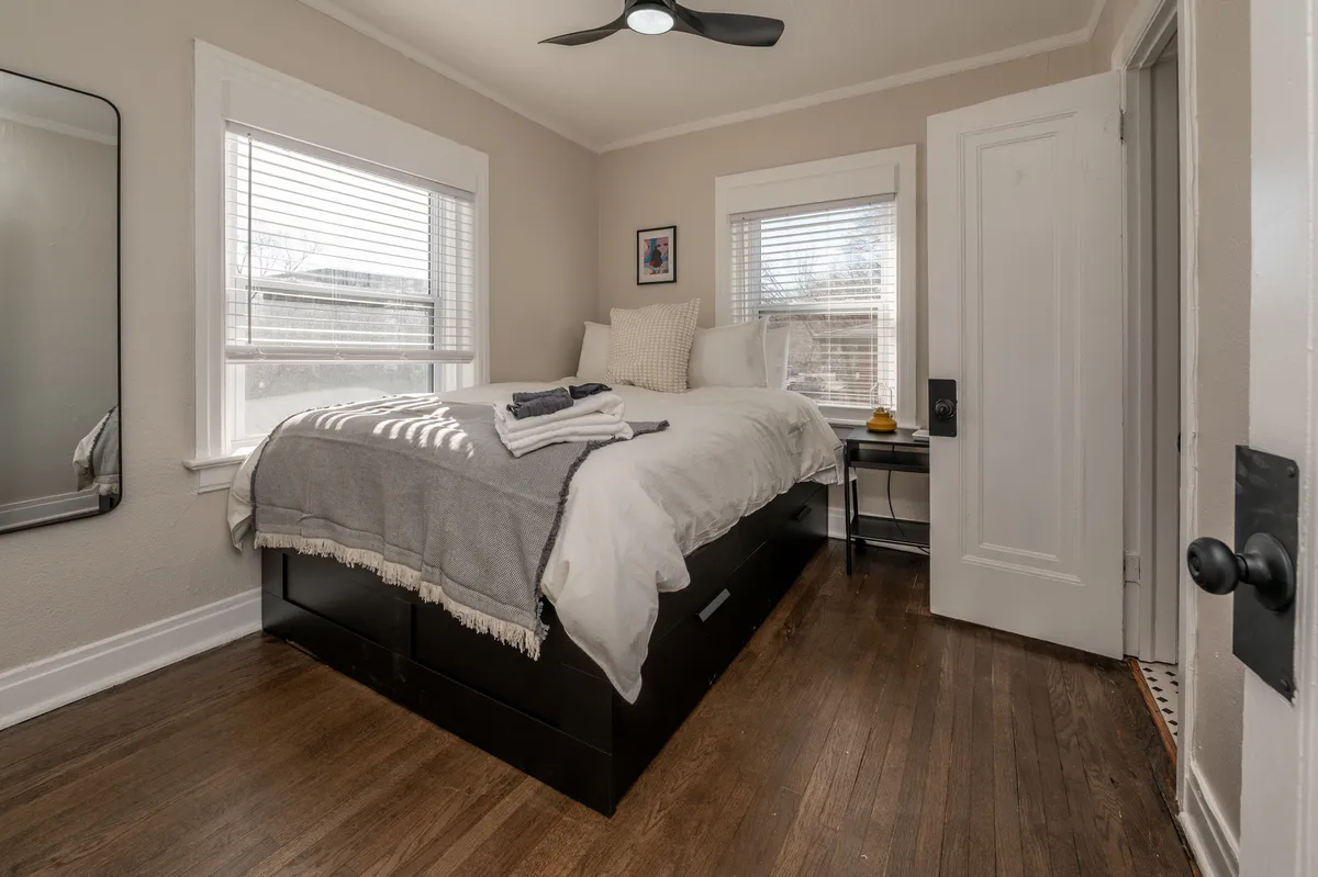 This image centers on a serene bedroom with a plush bed dressed in quality linens, a nightstand with bedside lighting, a stylish mirror, and calming wall art, all bathed in soft natural light. The overall atmosphere is peaceful and welcoming, providing a sense of tranquility.